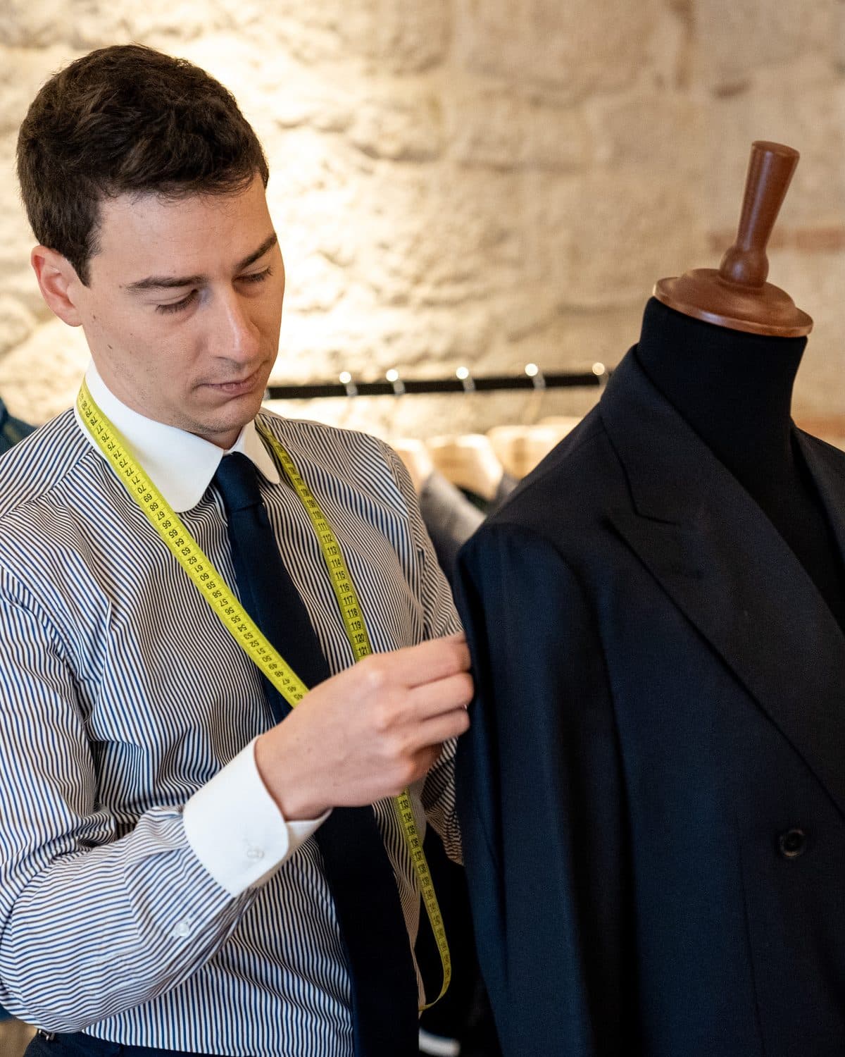 A tailor with a tape measure round his neck shaping a navy jacket on a form inside the Caprice Bespoke atelier in Italy