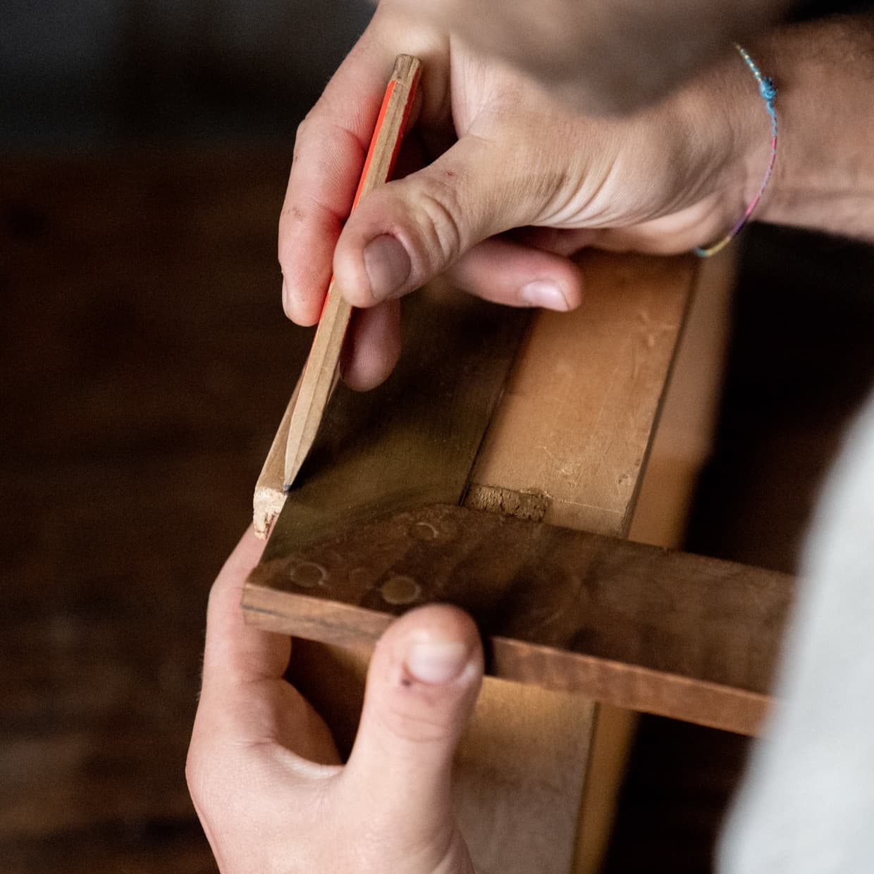 Hands marking a measurement on a wooden tailoring tool inside the atelier