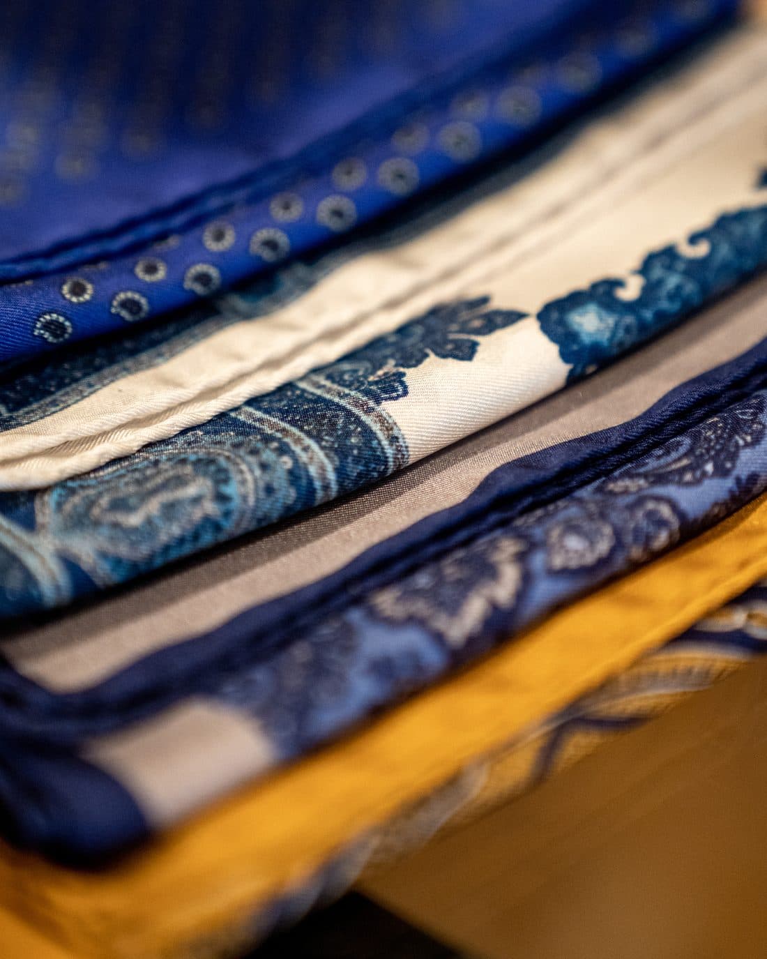 A stack of folded Italian silk cloth in blue paisley and stripe patterns