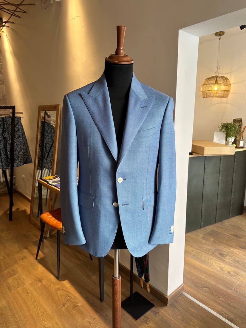 A light blue single-breasted jacket with peak lapels and patch pockets, finished on a dress form in the atelier
