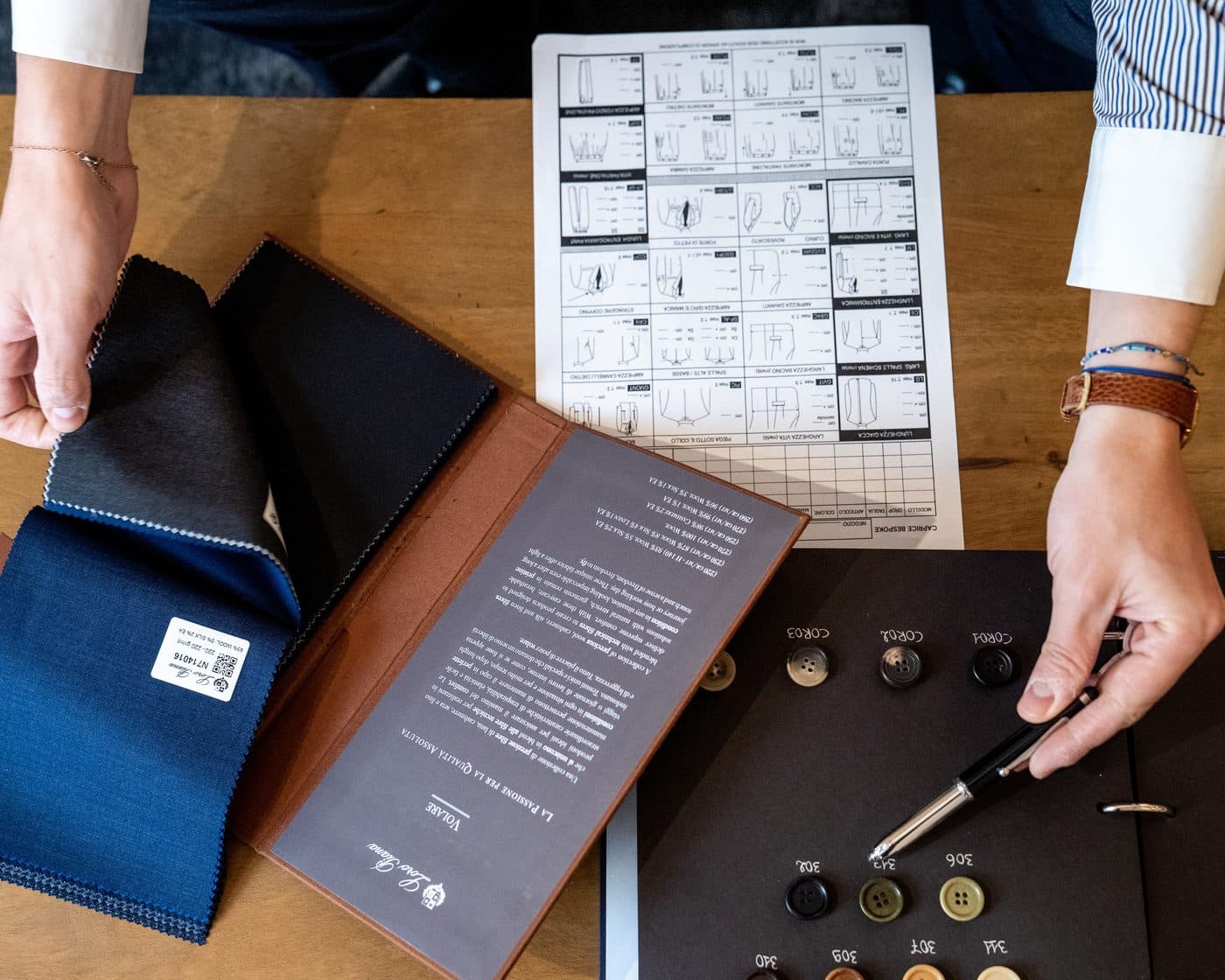 Fabric swatches, a garment specification sheet and a horn button tray laid out on a worktable while an order is specified